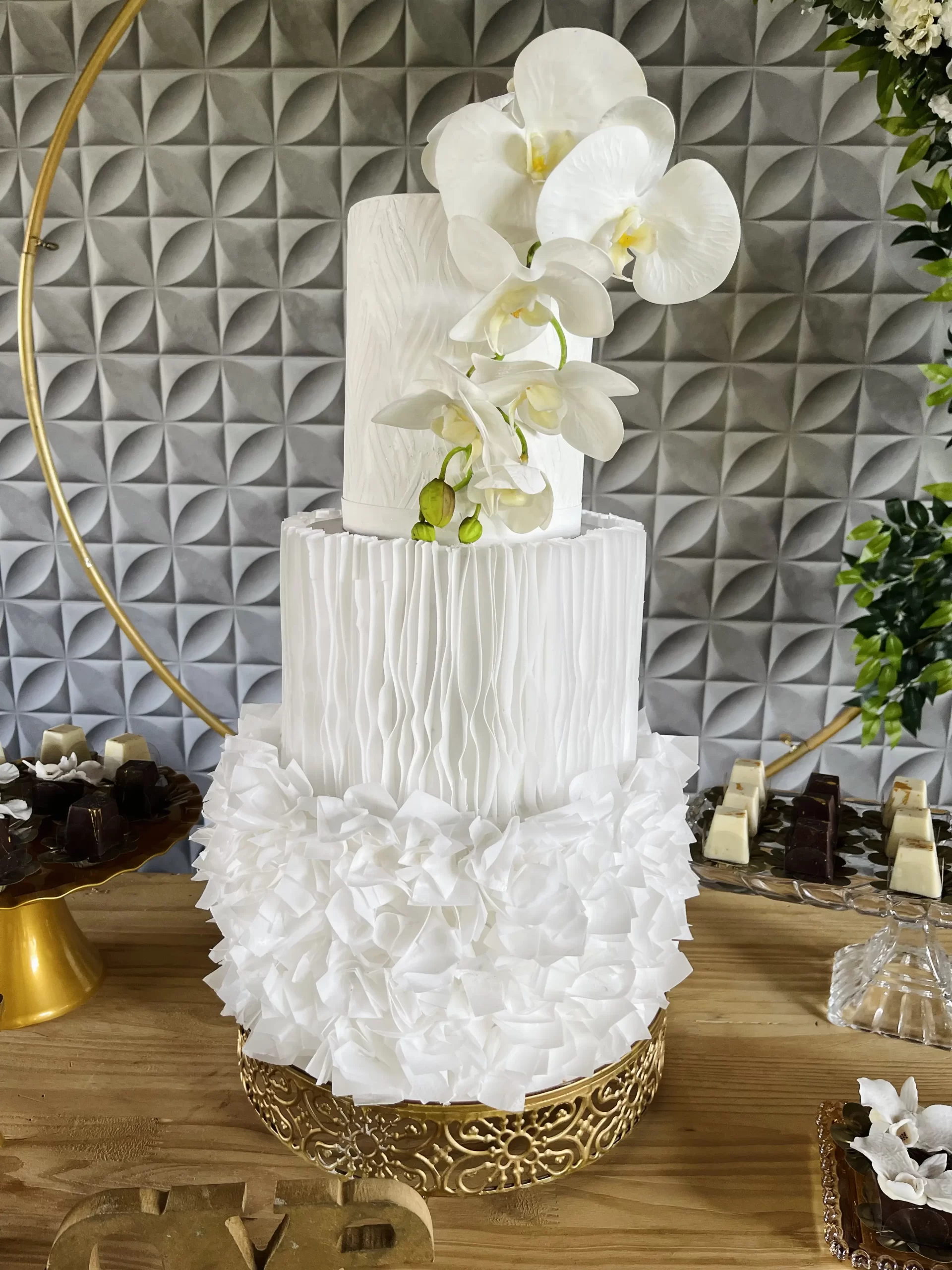 Bolo fake de casamento 3 andares branco com papel de arroz volumoso na base, textura plissada e orquídeas brancas.